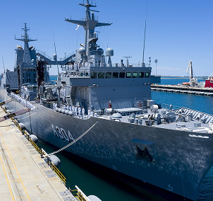 "Military naval vessel docked at a port with clear skies"