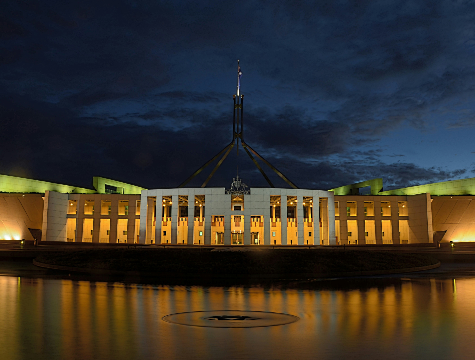 Parliament House in Canberra illuminated at night, reflecting in the water feature in front